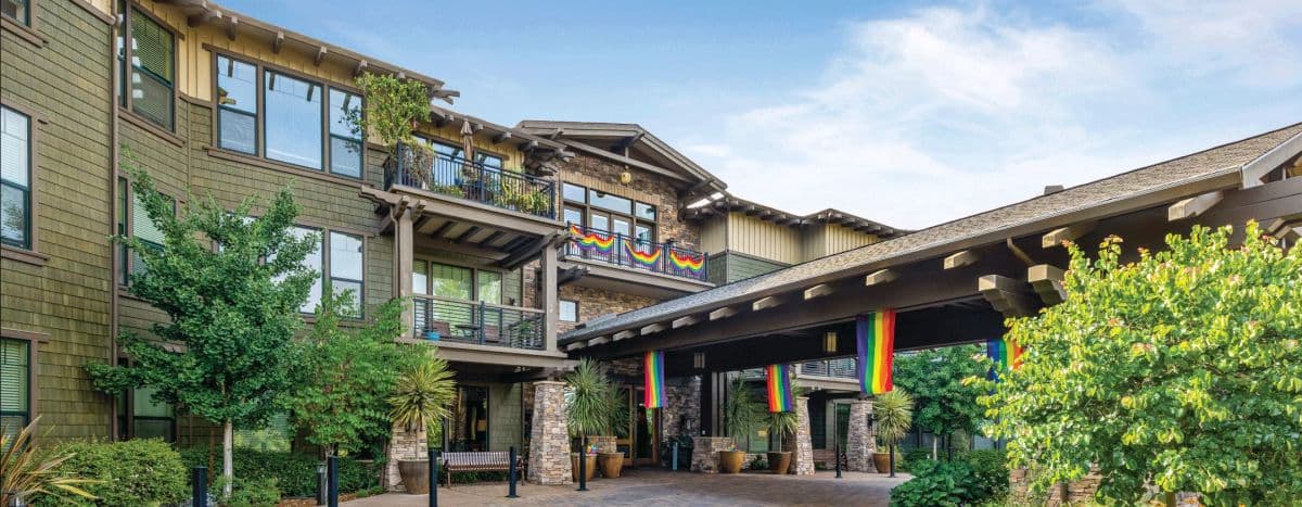 The entrance to Fountaingrove Lodge, a timber and stone building with rainbow flags hanging from the porte-cochere and upper balcony.