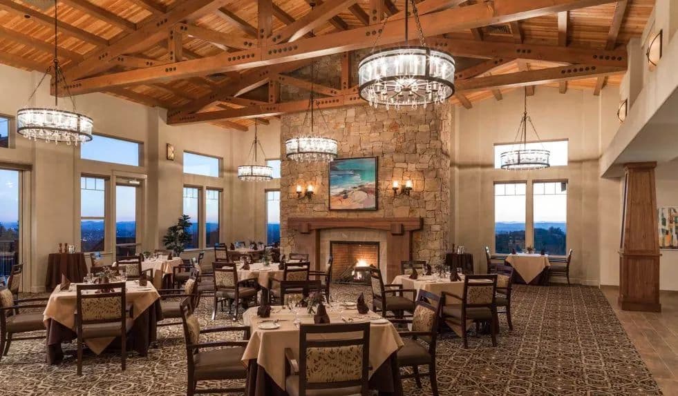 The dining room at Fountaingrove Lodge, with a vaulted timber ceiling, chandeliers and a tall stone fireplace between windows.